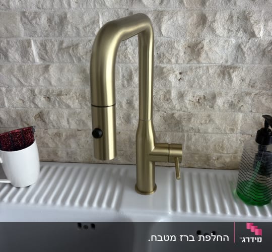 ברז זהב מותקן על כיור לבן עם קיר אבן ברקע